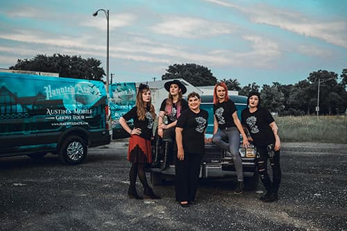 Haunted ATX team wearing HATX shirts while sitting on the hood of the black hearse next to the van