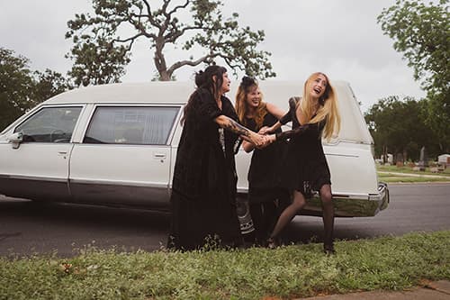 Two girls dressed pulling a third girl to the white hearse