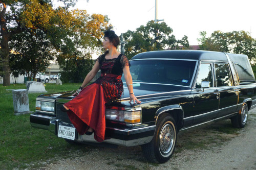 Women in red and black dress sitting on hood of black hearse