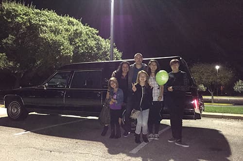 A family smiling happily in front of the hearse at the end of a spooky tour
