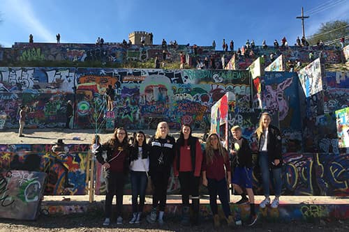 A teens standing smiling in front of graffiti on the Scavenger Hunt Tour