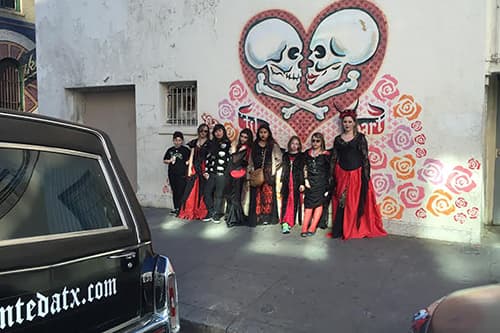Children's party all dressed in black and red attire in front of a mural of two skulls kissing