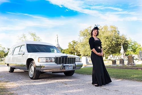 Woman in black dress standing in front of white hearse tour vehicle