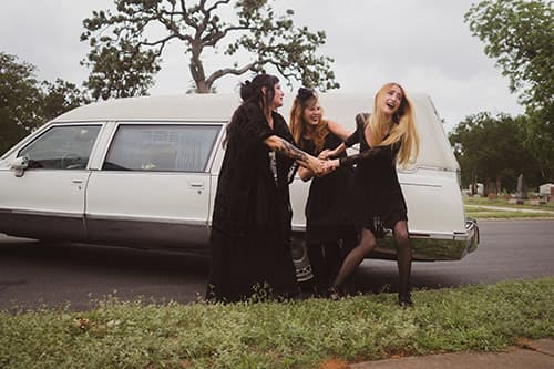 Two girls dressed pulling a third girl to the white hearse