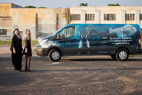 Two tour guides dressed in black standing to the side of the van