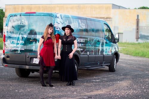 Two tour guides standing at the back of the van dressed in red and black